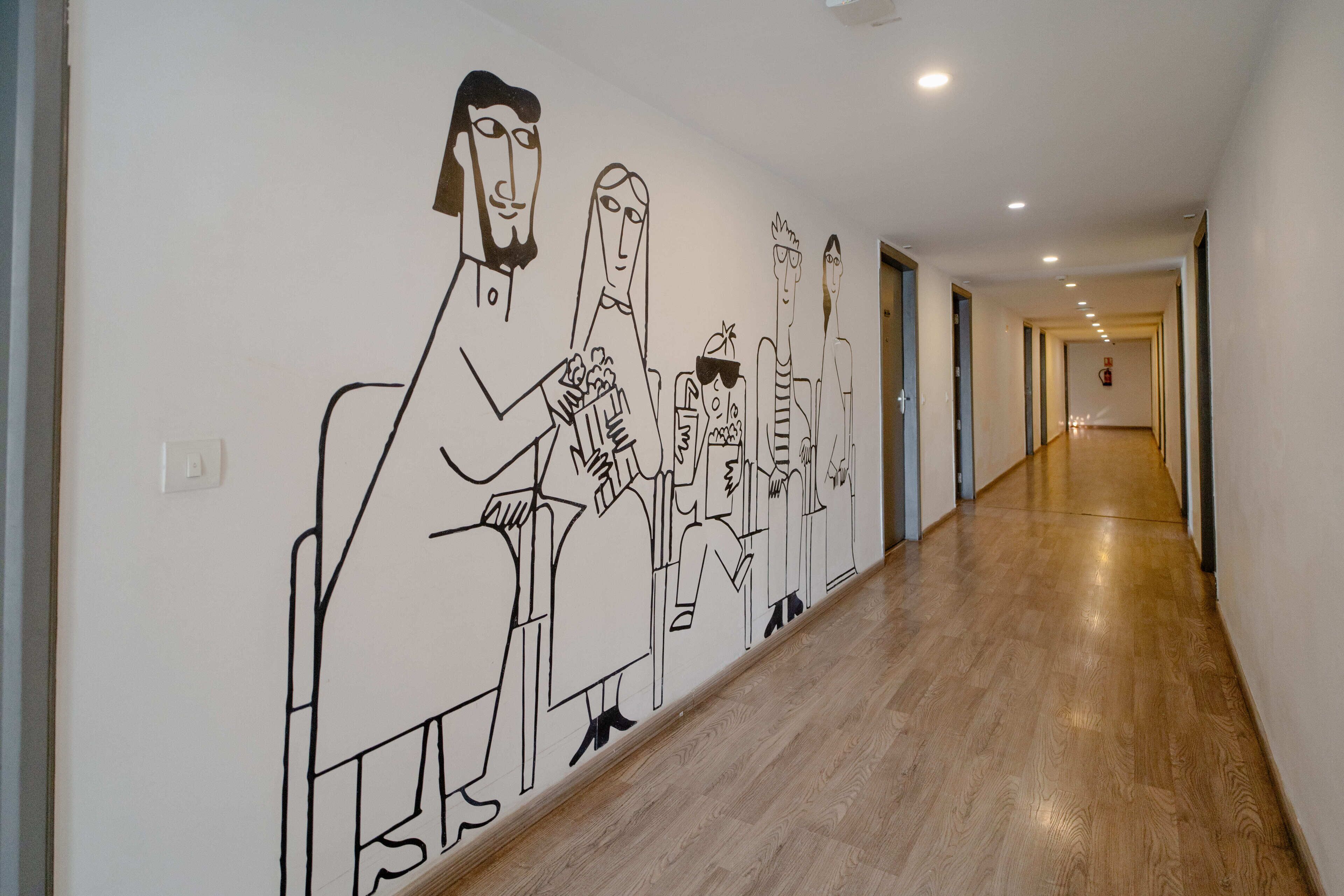 A hallway with a mural of abstract figures and a wooden floor.