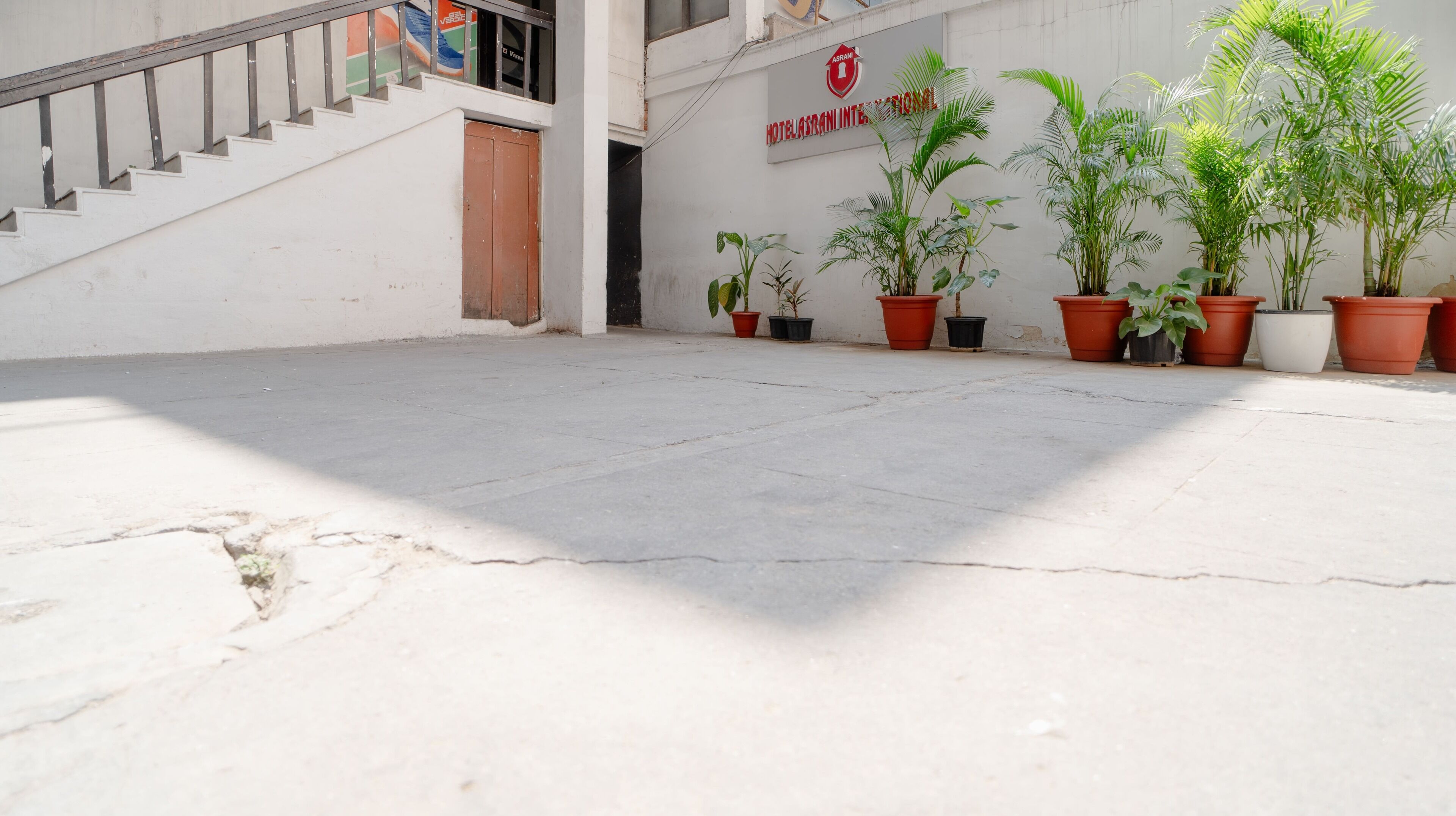 A courtyard with a staircase leading to a door, potted plants, and a sign for 'Hotel Asrani'.