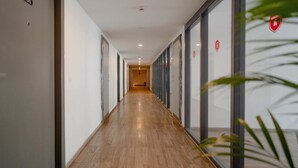 A long, narrow hallway with wooden flooring and glass doors on one side. - HOTEL ASRANI INTERNATIONAL (Hyderabad)