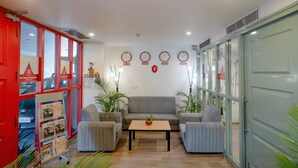 A hotel lobby with a red door, a grey sofa, two armchairs, a coffee table, and a wall with clocks showing different time zones. - HOTEL ASRANI INTERNATIONAL (Hyderabad)
