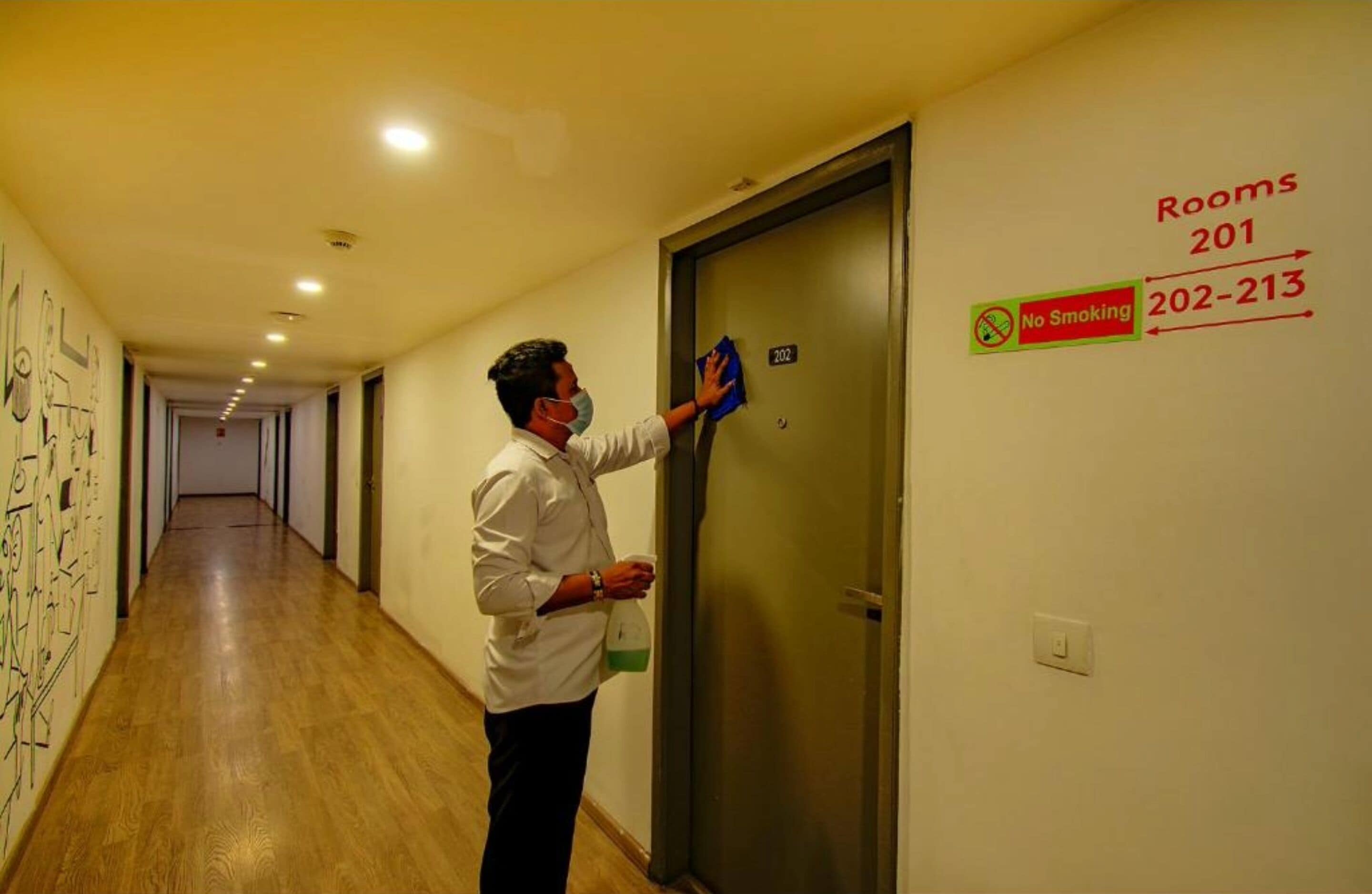 A hotel corridor with a person cleaning a door marked "Rooms 201" and "No Smoking" signs.
