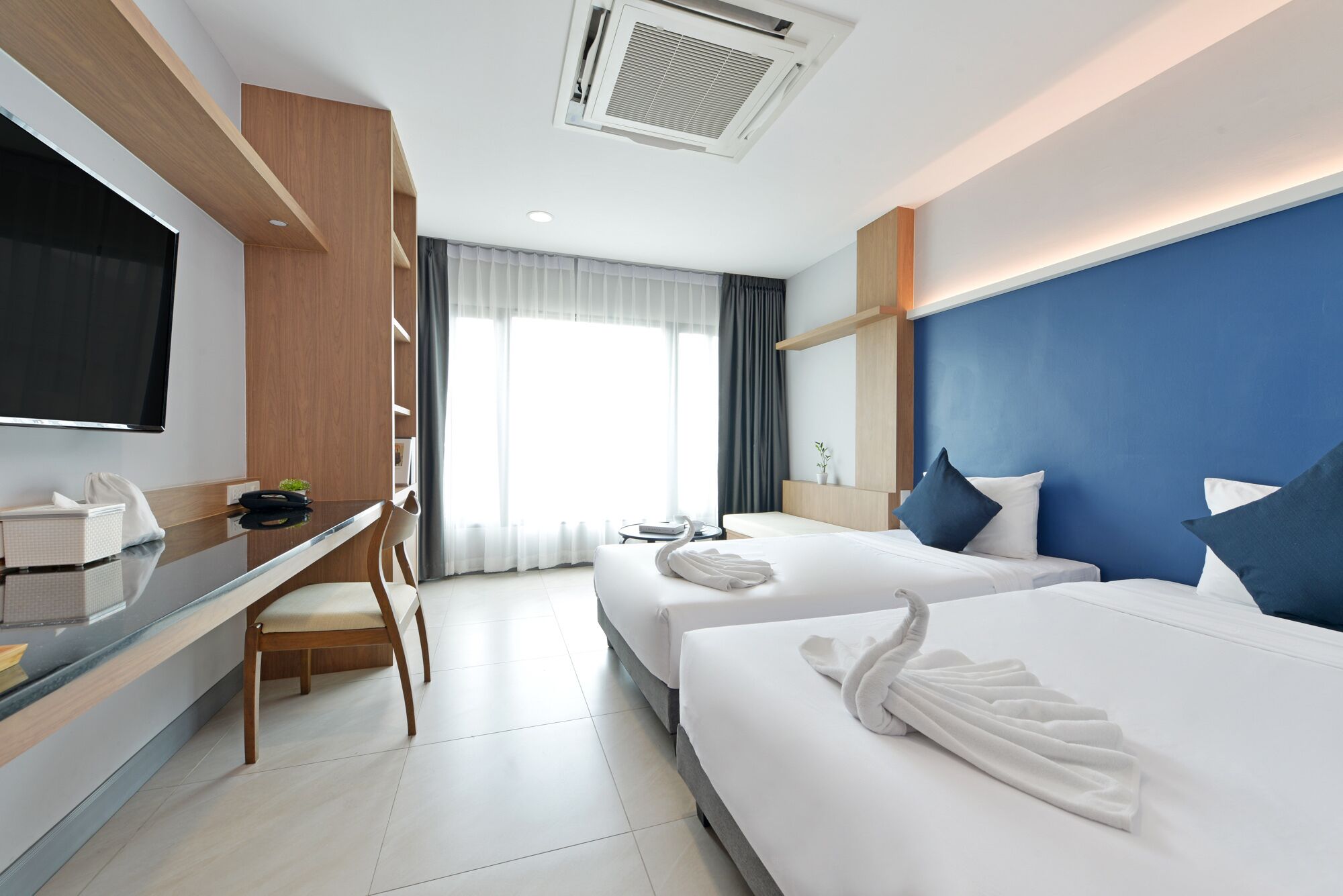 Habitación de hotel con dos camas, un escritorio, un televisor y una ventana con cortinas.