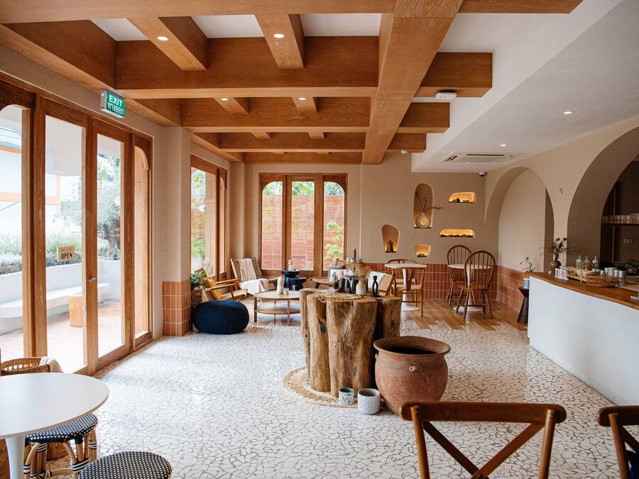 Un vaste espace intérieur doté de poutres en bois, de grandes fenêtres et d’un assortiment de différents types de sièges, notamment des tables et des chaises.