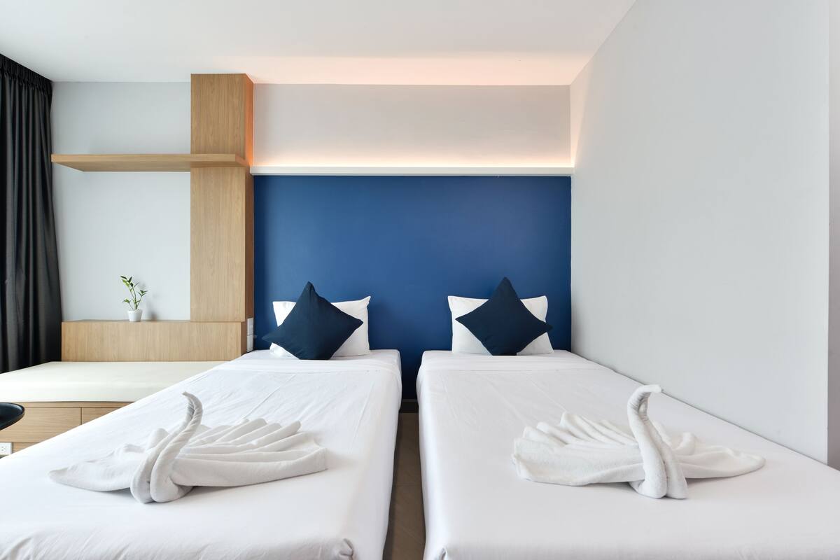 A hotel room with two single beds, a wooden headboard, a desk, and a small potted plant.