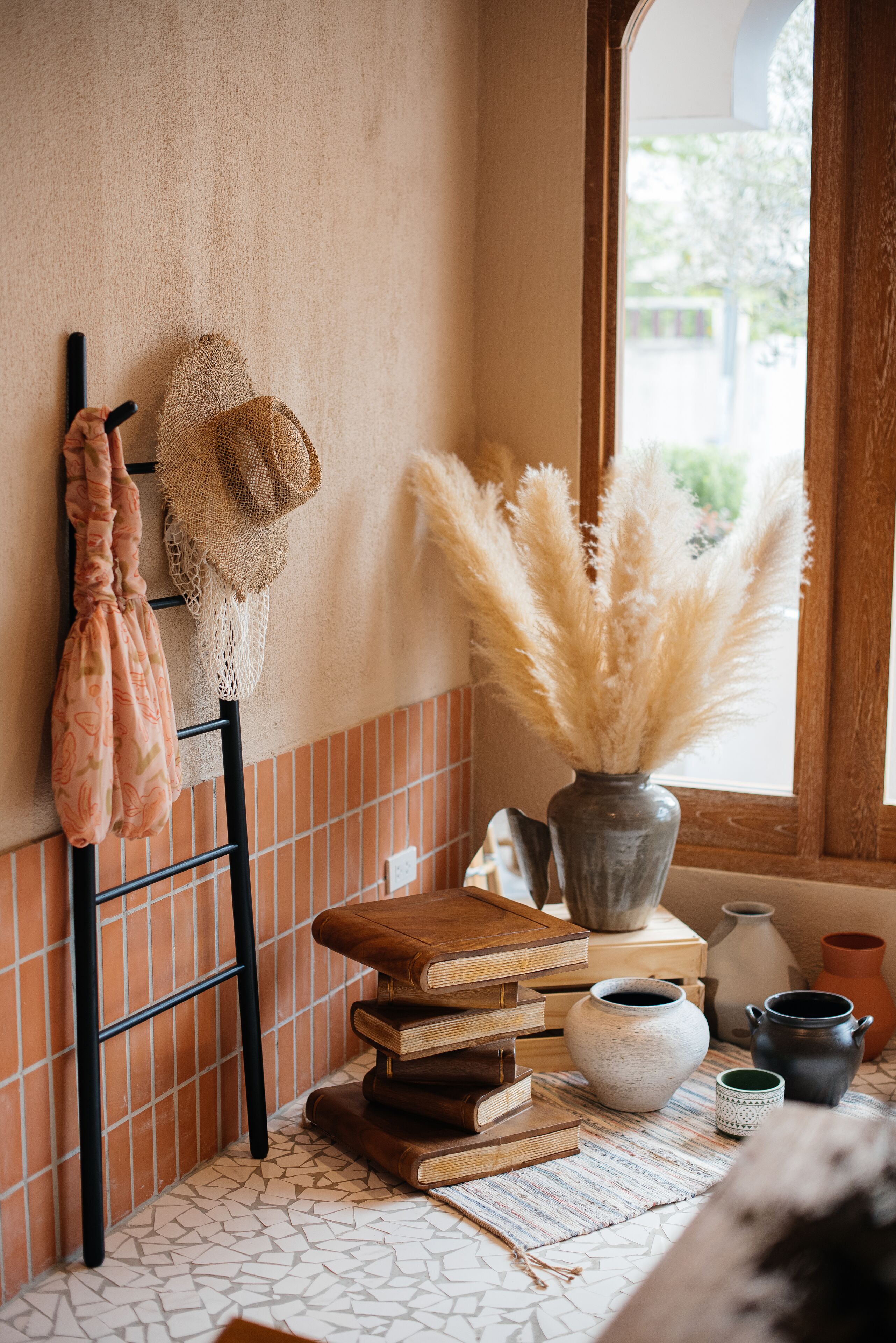 A cozy corner with a rustic shelf holding books, a woven bag, and a vase with pampas grass.