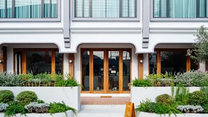 A modern building with a white facade, large glass doors, and a small garden area with various plants. - VST Punnawithi (Bangkok)