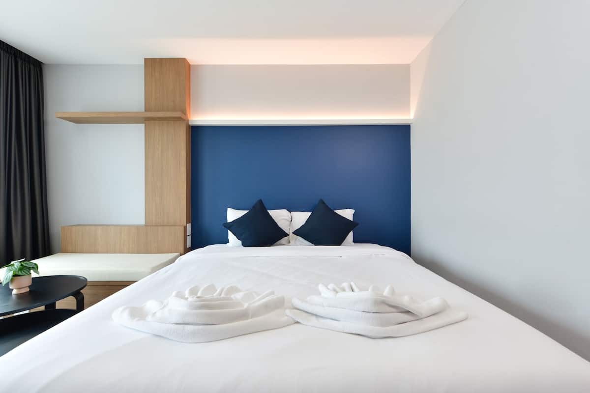 A hotel room with a bed, a bedside table with a plant, and a headboard with two pillows.