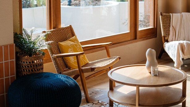 A cozy room with a large window, wicker chairs, a round wooden table, and a blue ottoman. - VST Punnawithi (Bangkok)