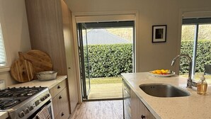Une cuisine moderne dotée d’un grand îlot central, d’appareils électroménagers en acier inoxydable et d’une porte-fenêtre coulissante donnant sur un jardin.