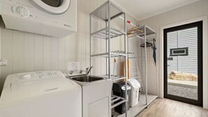 Une buanderie équipée d’un lave-linge, d’un étendoir et d’une étagère où sont rangés les vêtements et les produits de nettoyage.