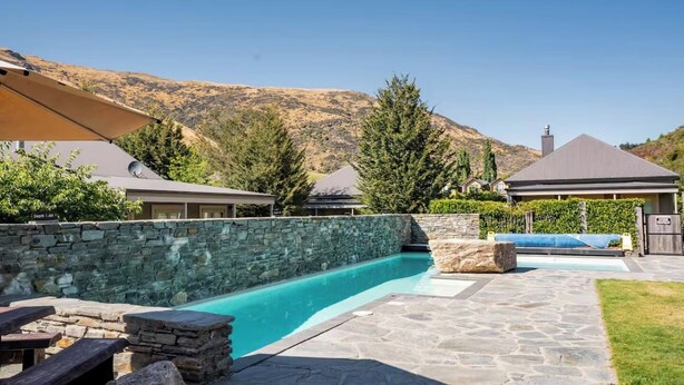 Un jardin avec une piscine, des murs en pierre et des maisons aux toits inclinés.