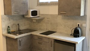 Een kleine keuken met een ingebouwde magnetron, een spoelbak en een koffiezetapparaat.