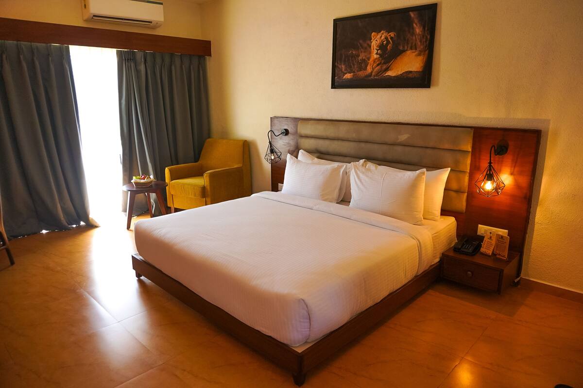 Quarto de hotel com uma cama grande, uma mesa de cabeceira com abajur, uma cadeira e um quadro na parede.