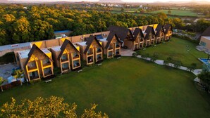 A row of modern, uniquely designed buildings with multiple balconies, surrounded by lush greenery and a well-maintained lawn. - Jagira Ananta Elite Gir (Talala)