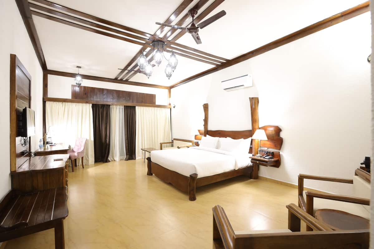 Quarto de hotel com cama de madeira, uma escrivaninha, uma cadeira, ventoinha no teto e um lustre.