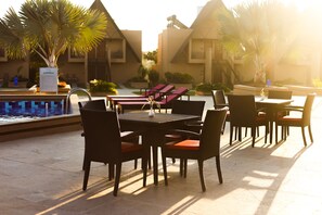 A poolside area with lounge chairs, a table, and chairs. - Jagira Ananta Elite Gir (Talala)