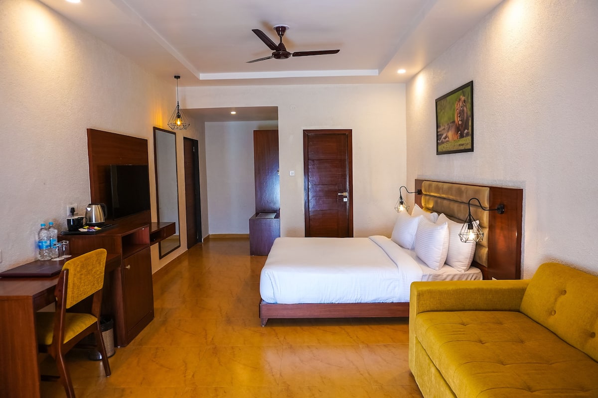 Quarto de hotel com cama, escrivaninha, cadeira, sofá, televisão e ventoinha no teto.