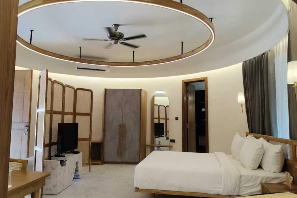 Quarto de hotel moderno com teto curvo, uma cama, TV, guarda-roupa e espelho.