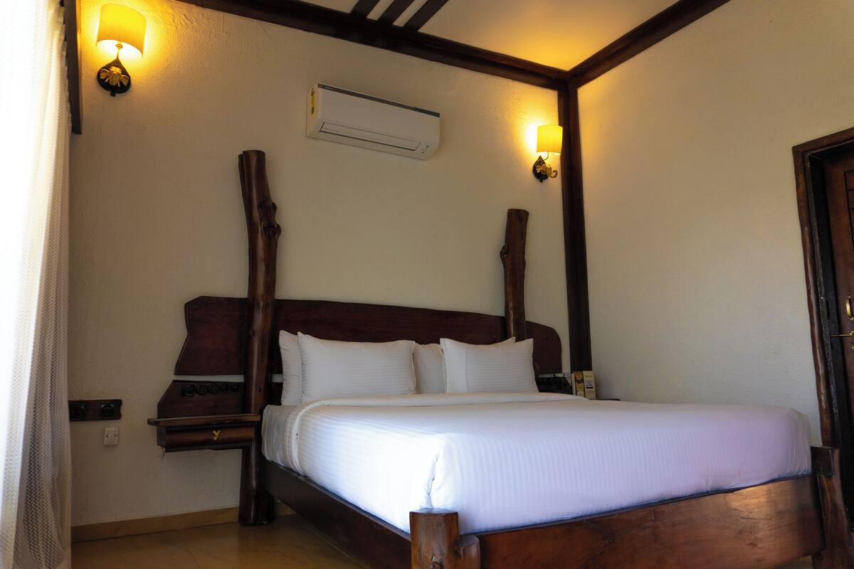 Quarto com cama de madeira, duas mesas de cabeceira, ar-condicionado fixado na parede e duas luminárias de parede.