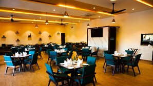 A spacious restaurant with multiple dining tables and chairs, ceiling fans, and a flat-screen TV mounted on the wall. - Jagira Ananta Elite Gir (Talala)
