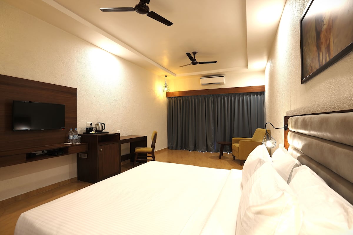 Quarto de hotel com cama, escrivaninha com televisão, cadeira, ventoinha no teto e aparelho de ar condicionado.