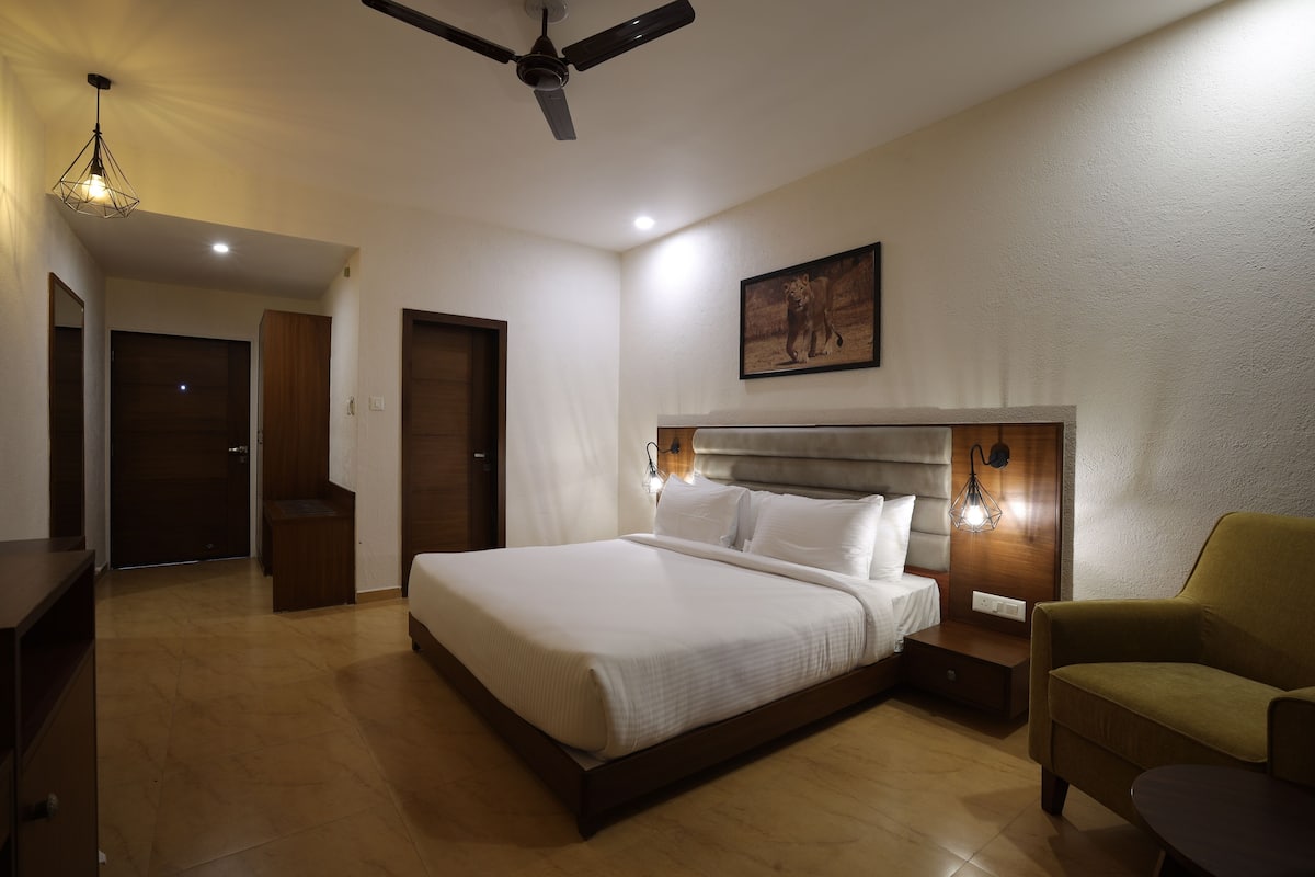 Quarto de hotel com uma cama grande, um ventilador de teto, uma mesa de cabeceira, uma cadeira e um quadro na parede.