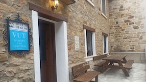 Un bâtiment en pierre avec une porte en bois, une enseigne et des bancs en bois à l’extérieur.