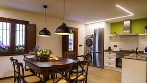 Une cuisine moderne avec une table à manger en bois, des chaises, des luminaires suspendus, un lave-linge, un réfrigérateur et un mur d’accent vert.