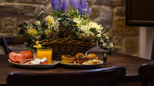 Une table à manger avec un panier de fleurs, des assiettes remplies de nourriture et un verre de jus d’orange.