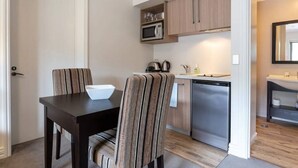 A compact kitchen with a microwave, kettle, and dishwasher. There is a dining table with chairs and a bowl on it. - Studio 25 - 1 Bedroom place with Pool (Cardrona)