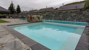 A rectangular swimming pool with a stone border, set against a stone wall with a chimney. - Studio 25 - 1 Bedroom place with Pool (Cardrona)