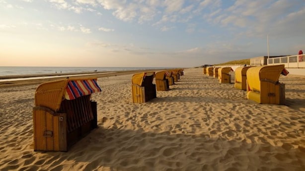 En strand med rækker af strandstole og parasoller, en sandet kystlinje og havet i baggrunden.