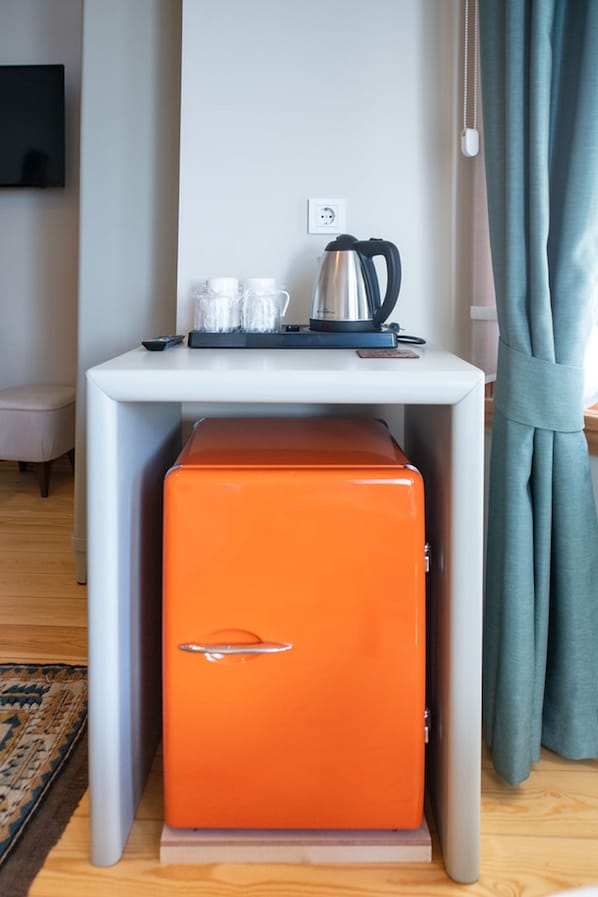 Habitación compacta con una mesa blanca, un mueble naranja, una tetera y un enchufe en la pared.
