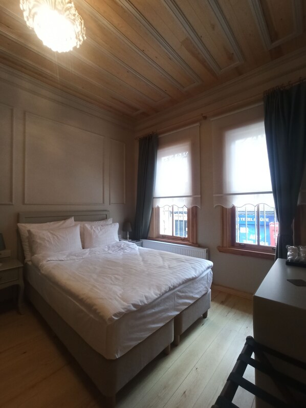 Un dormitorio con una cama grande, techo de madera, dos ventanas con cortinas y un radiador.