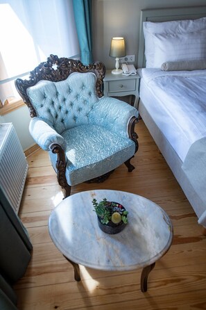 A hotel room with a classic blue armchair, a white bed, a bedside table with a lamp, and a small table with a decorative item. - İkiz Konak Boutique Hotel (Istanbul)