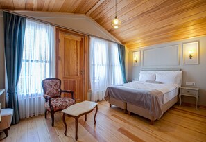 Un dormitorio con techo de madera, una cama, una silla, una mesa y cortinas.