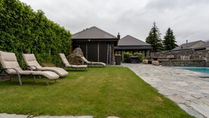 A backyard with a stone patio, a swimming pool, and a covered outdoor area with lounge chairs. - Studio 26 - One Bedroom Place with Pool (Cardrona)