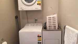 A laundry area with a washing machine, a dryer, and a stacked washer and dryer unit. - Studio 26 - One Bedroom Place with Pool (Cardrona)