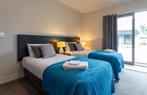 Two beds with headboards and pillows, each with bedside lamps, offer a comfortable retreat with a view of the outside through large windows.
