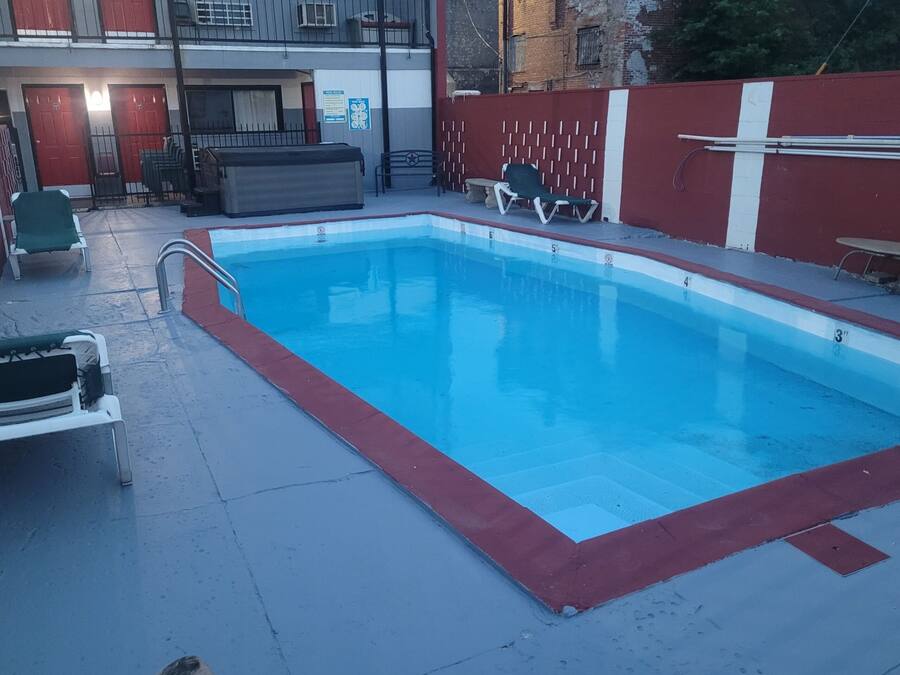 A rectangular swimming pool with a red border, surrounded by a concrete deck. There are lounge chairs and a bench near the pool.