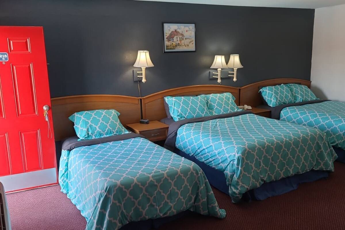 Ein Hotelzimmer mit drei Betten, einer roten Tür und zwei Wandlampen.