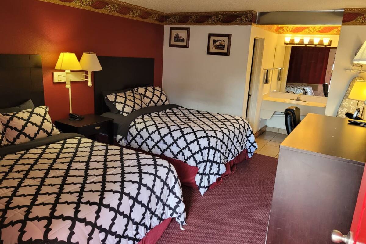 Ein Hotelzimmer mit zwei Betten, einem Schreibtisch, einem Spiegel und einem roten Teppich.