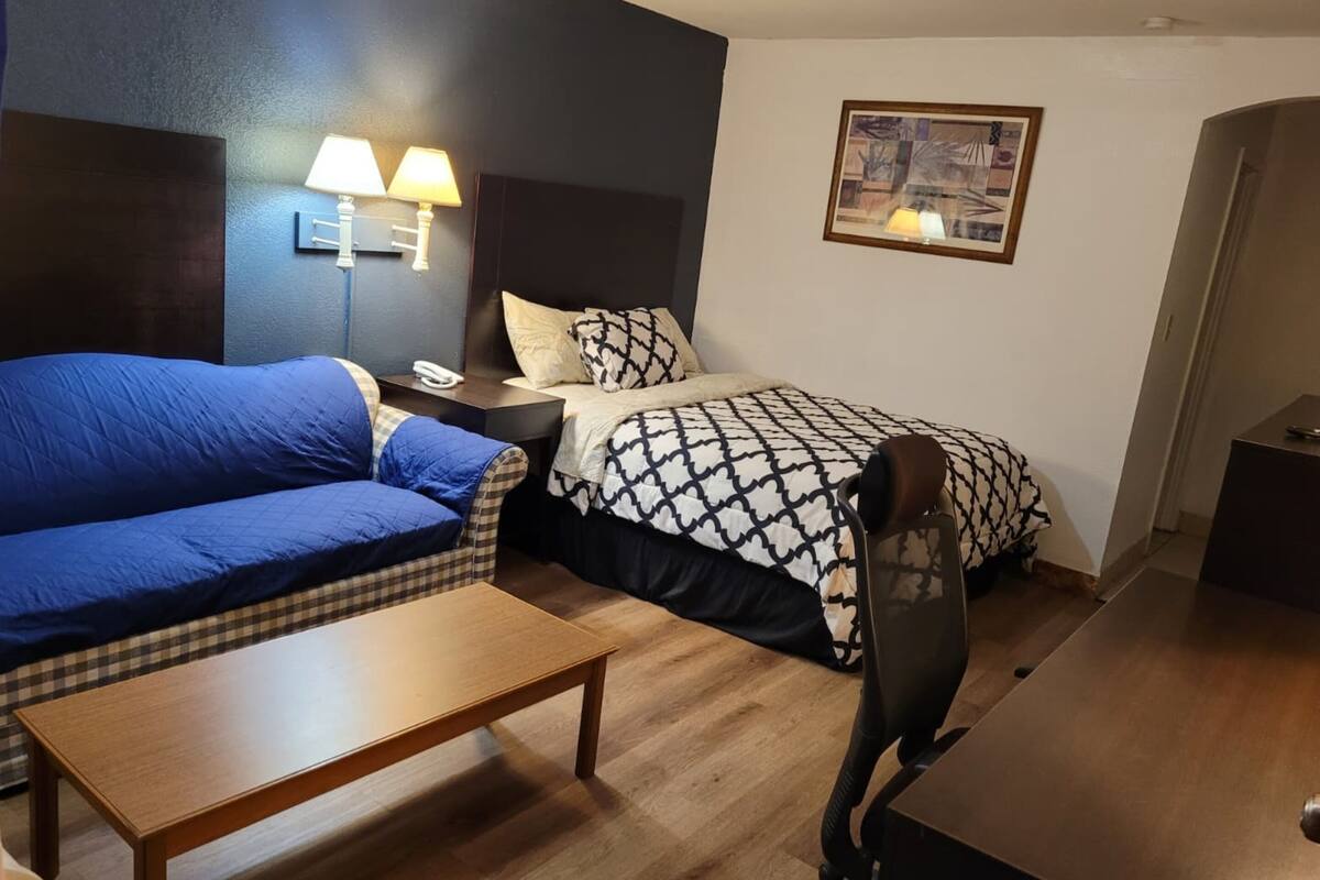 Ein Hotelzimmer mit blauer Couch, einem Bett mit gemusterten Textilien, einem Holztisch und einem Schreibtisch mit Stuhl.