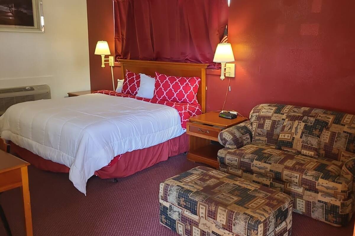 Ein Hotelzimmer mit einem Bett, einem Holznachttisch, einer roten gepolsterten Couch und einem gemusterten Hocker.