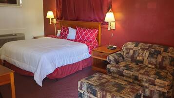 A hotel room with a bed, a wooden nightstand, a red upholstered sofa, and a patterned ottoman.