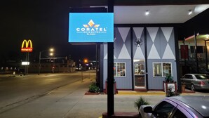 Een hotel genaamd 'Coratel Inn & Suites' met een blauw bord, een McDonald's bord op de achtergrond en een parkeerplaats.