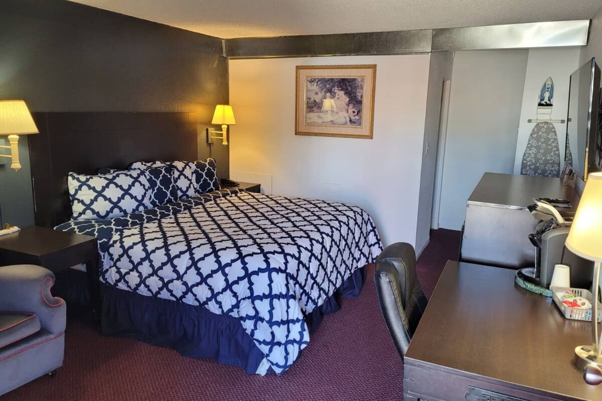 Ein Hotelzimmer mit einem großen Bett, einem Schreibtisch mit Stuhl, einem kleinen Tisch und einer Lampe.