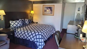 Een hotelkamer met een groot bed, een bureau met stoel, een bijzettafeltje en een lamp.