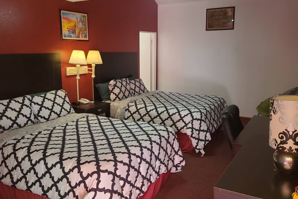 Ein Hotelzimmer mit zwei Betten, jeweils mit gemusterten Laken, einem Nachttisch mit Lampen, einem Tisch mit einer Vase und Bildern an den Wänden.