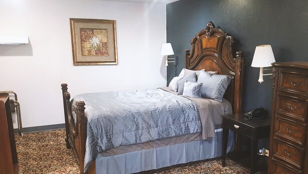 Een slaapkamer met een houten bed, een kamerbreed tapijt, een dressoir en een wandlamp.